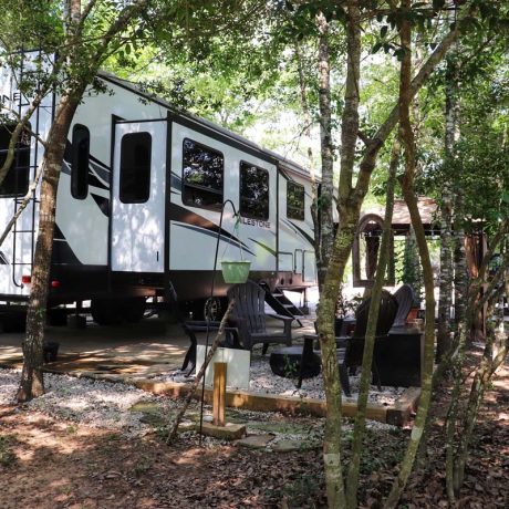 rv parked with seating outside surrounded by trees